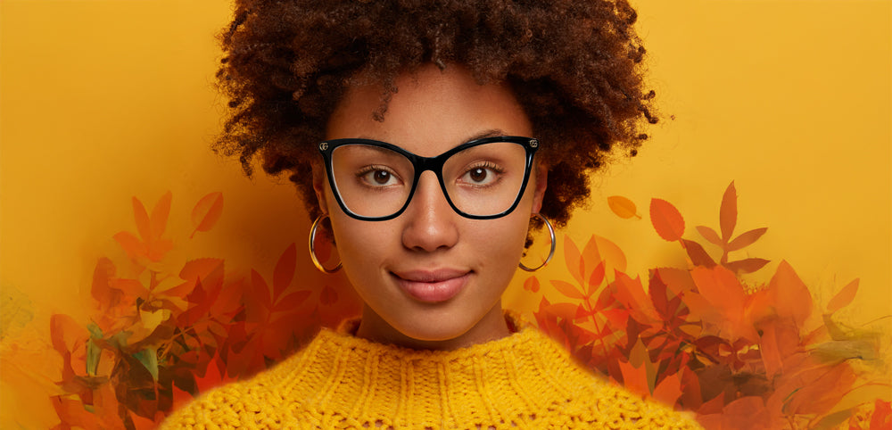 Woman wearing glasses and a yellow sweater with autumn leaves in the background
